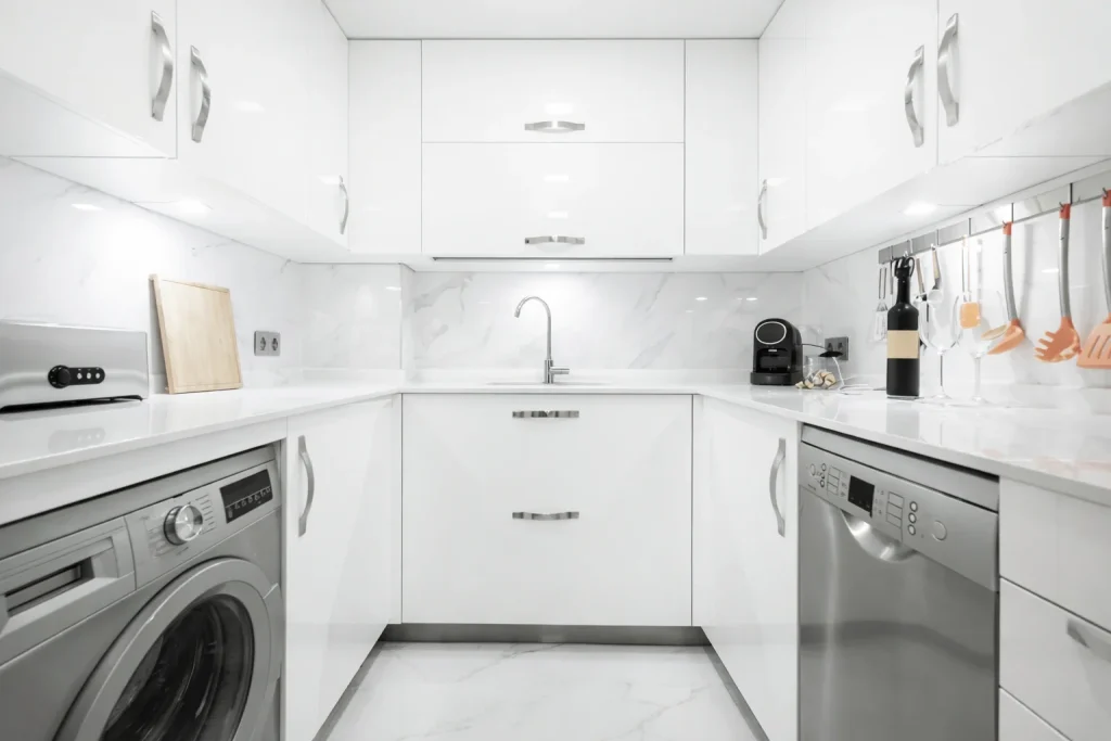 Modern white modular kitchen with marble countertop, built-in appliances, and storage cabinets