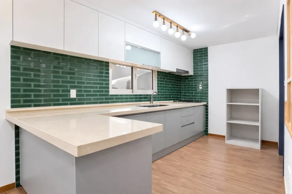 Modern kitchen interior with green subway tile backsplash, white cabinets, and quartz island