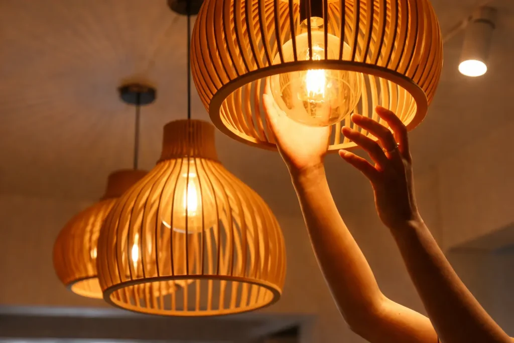 Person adjusting warm glowing wooden pendant light with exposed filament bulb