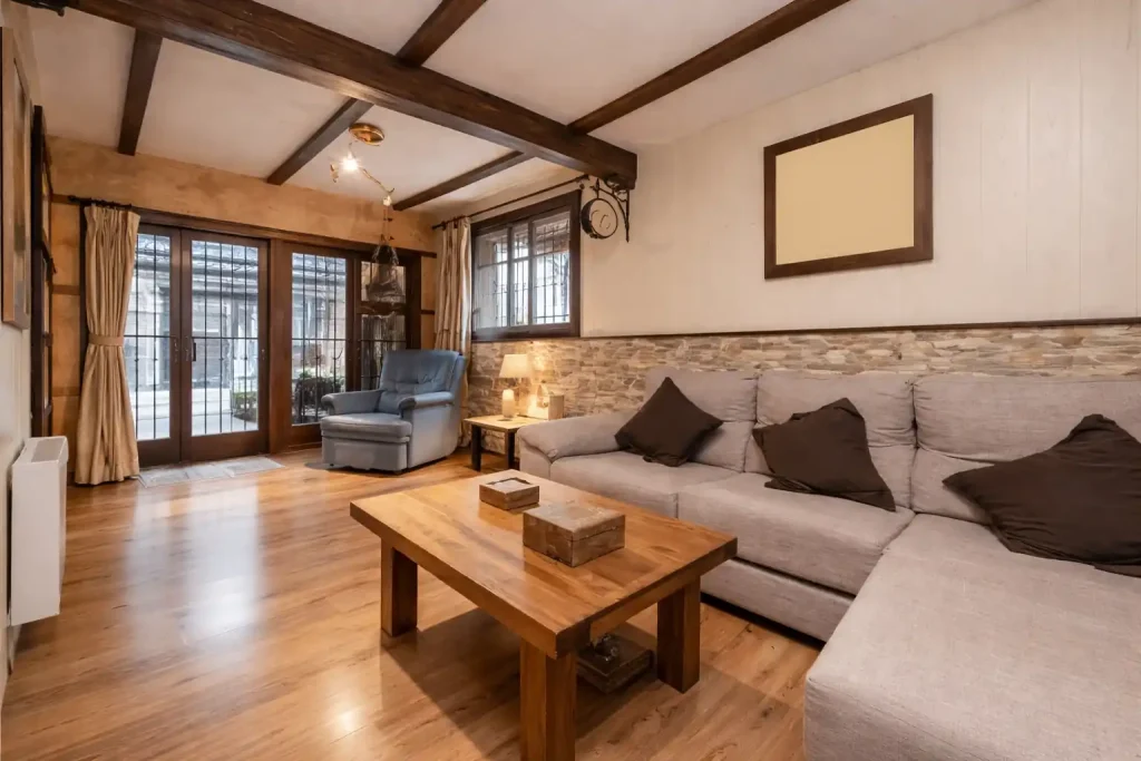 Rustic living room interior with exposed wooden beams, cozy sofa, wooden coffee table, and large glass doors