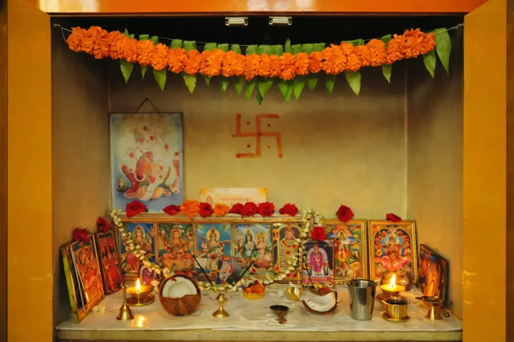 Wall-mounted pooja room design with Ganesh idol, framed Hindu deities, marigold garlands, diyas, and traditional decor