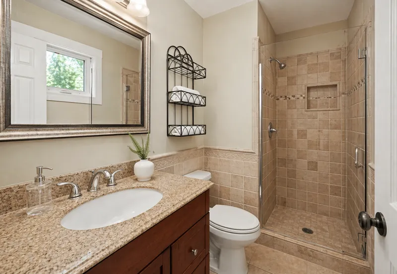 Small bathroom with bathtub shower combo, wooden vanity cabinet, granite countertop, and decorative mirror