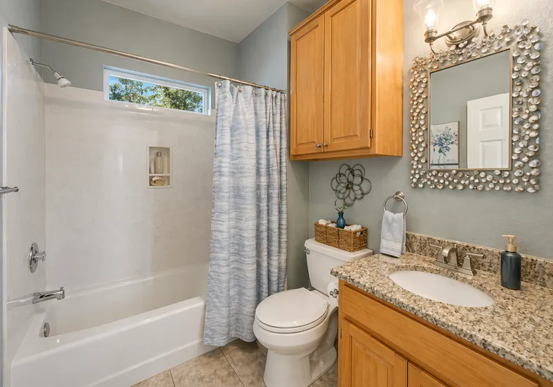 Small bathroom with bathtub shower combo, wooden vanity cabinet, granite countertop, and decorative mirror