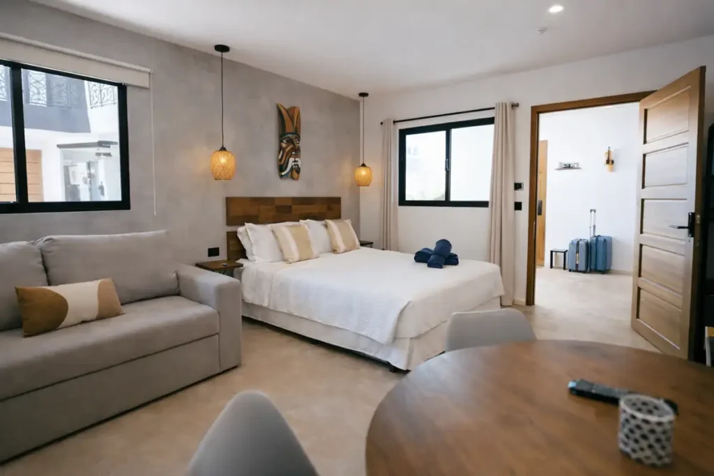 Modern bedroom with queen bed, sofa seating, wooden furniture, warm pendant lighting, and natural daylight