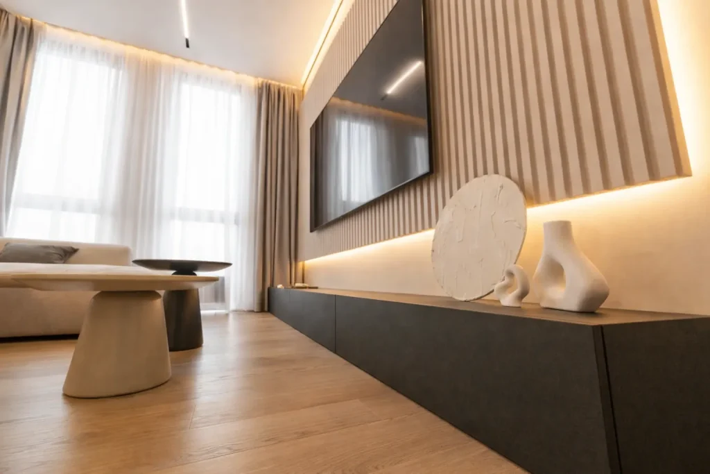 Modern living room with wall-mounted TV, wooden panel wall, soft lighting, beige sofa, and minimalist decor